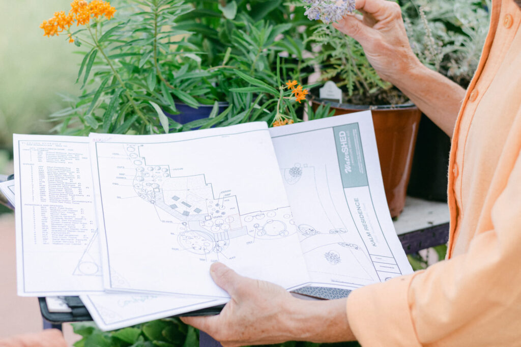 lady holding landscape architectural plans and other hand on pot of flowers