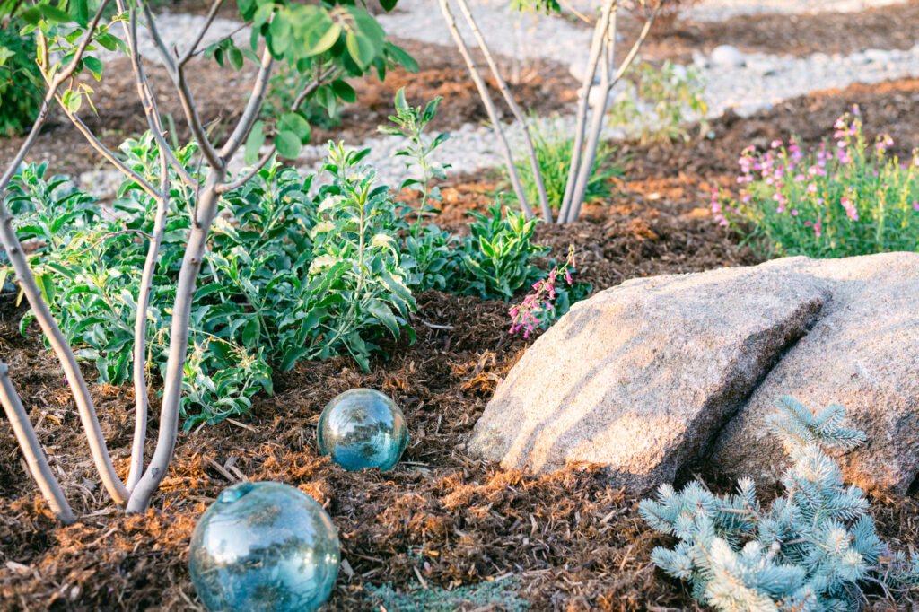 closeup of landscaping in yard with shrubs, rock, bushes, mulch and turquoise glass spheres