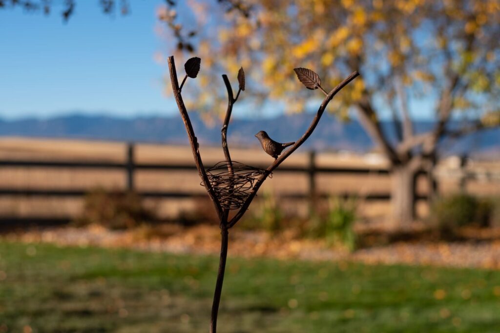 copper sculpture of birds and nest with grass fence and mountains in the background